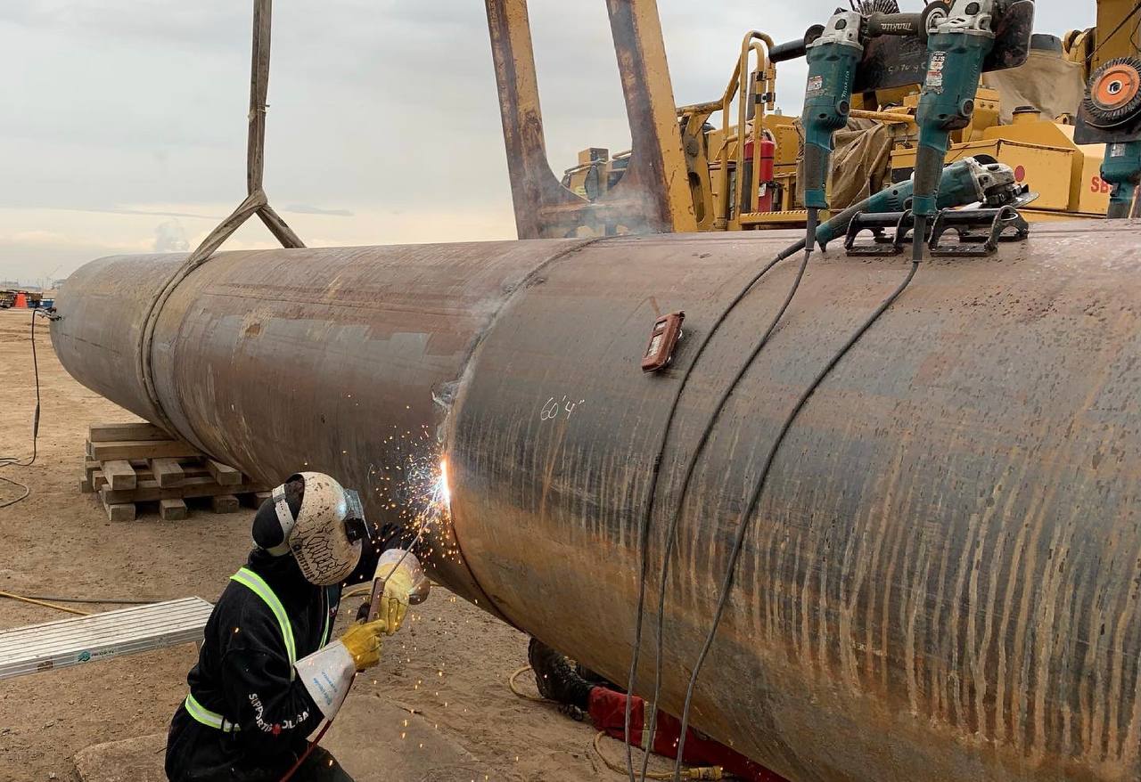 Dakota welding a horizontal pipe on a Calgary industrial site, sparks flying