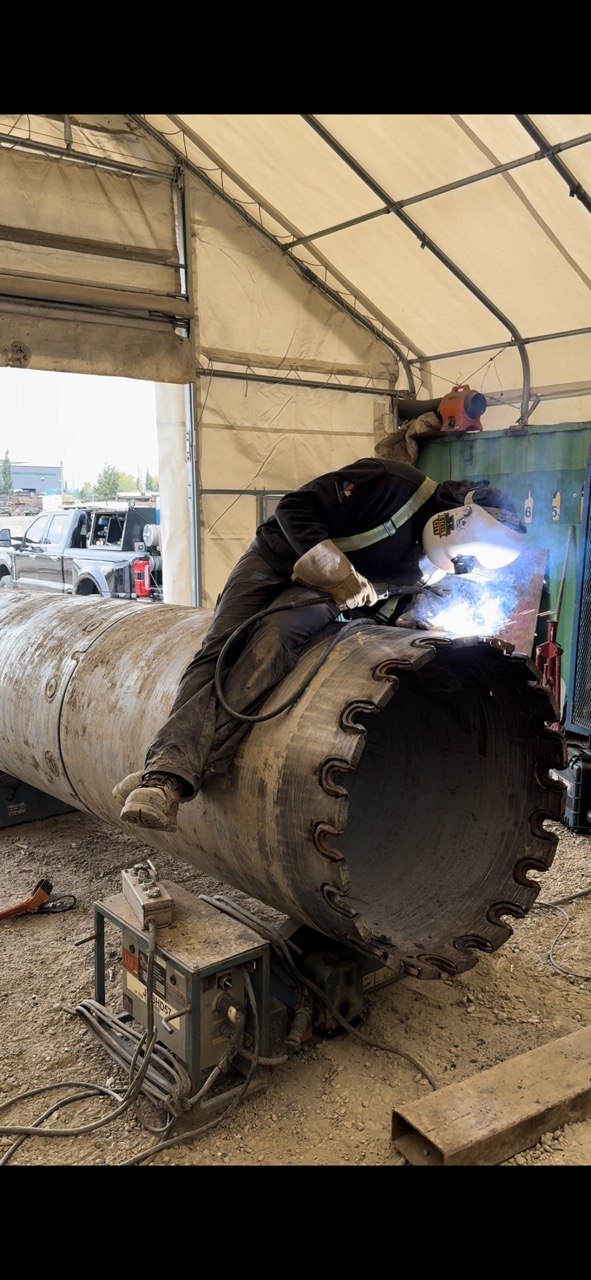 Dakota welding a large pipe assembly under cover, sparks flying